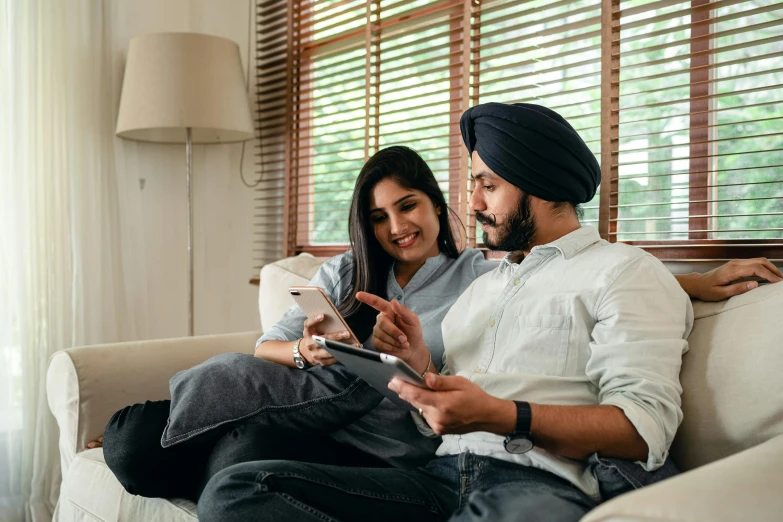 a man and woman sitting on a couch looking at a tablet, inspired by Manjit Bawa, trending on pexels, profile pic, australian, thumbnail, holds a smart phone in one hand