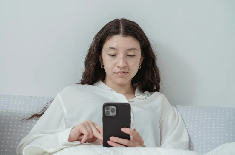 a woman sitting on a bed looking at her cell phone, trending on pexels, renaissance, without makeup, avatar image, white, black