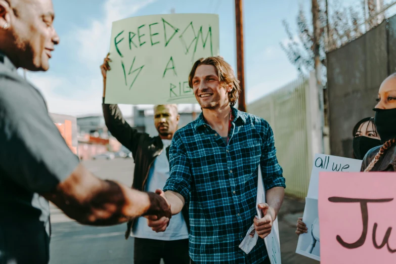 a man shaking hands with another man holding a sign, a photo, trending on pexels, freedom fighter, jamie campbell bower, group of people, a person standing in front of a