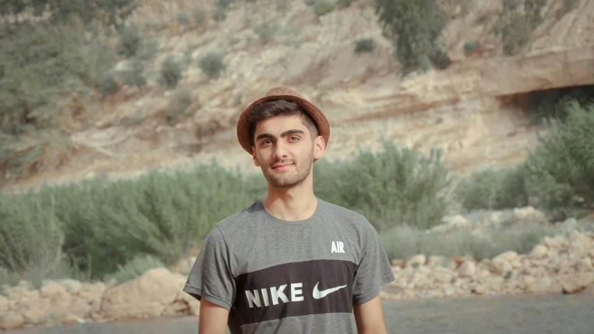 a man wearing a hat and holding a skateboard, a picture, by Ismail Acar, les nabis, standing in front of a mountain, headshot profile picture, slight cute smile, assyrian