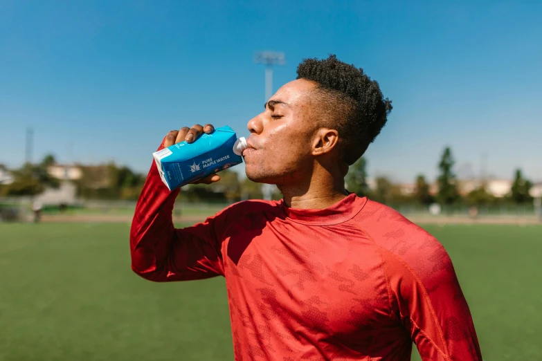 a man in a red shirt is drinking water, pexels contest winner, on a soccer field, vibrant blue, athletic muscle tone, profile image