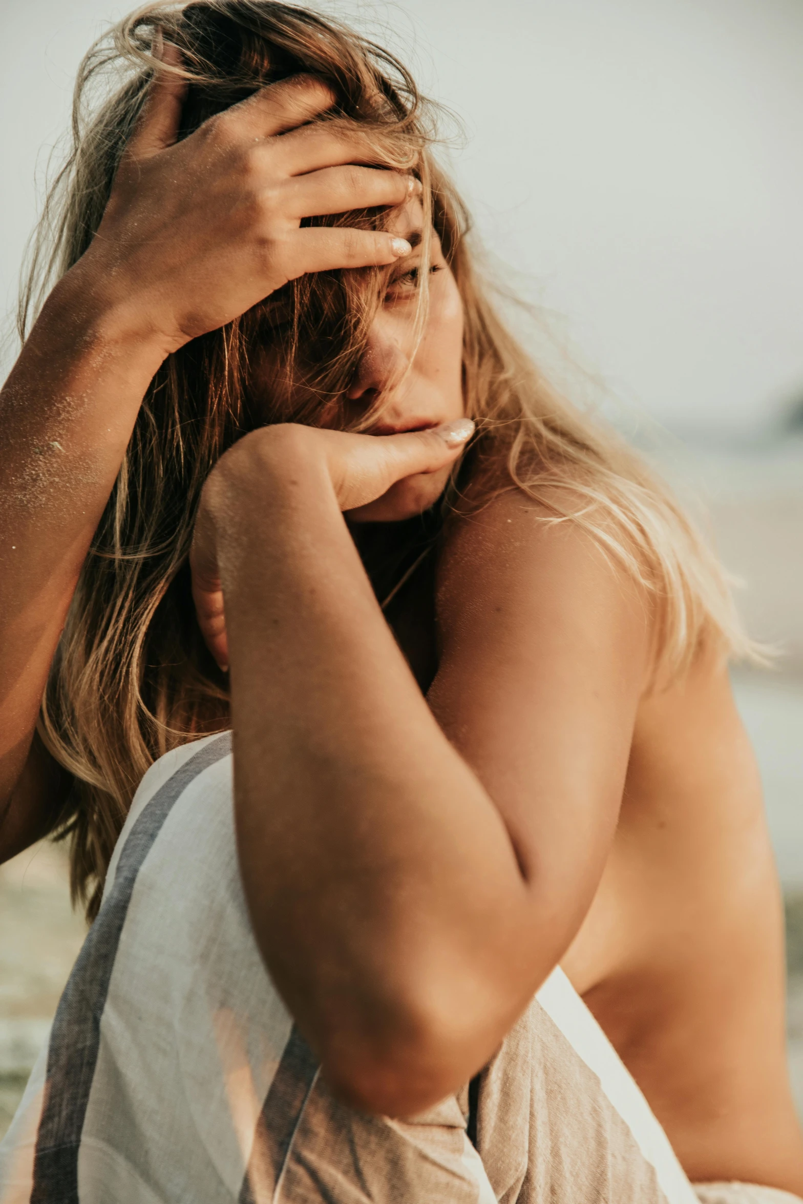 a woman sitting on top of a sandy beach, by Matija Jama, trending on pexels, closeup of sweating forehead, touching heads, looking her shoulder, dirty blonde hair