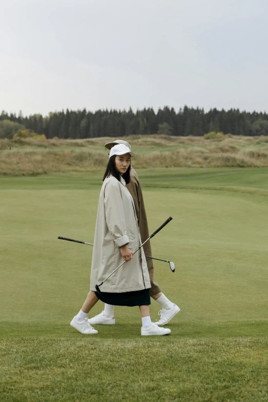 a woman walking across a lush green golf course, a picture, unsplash, renaissance, wearing a long coat, wearing off - white style, wearing japanese techwear, clubs