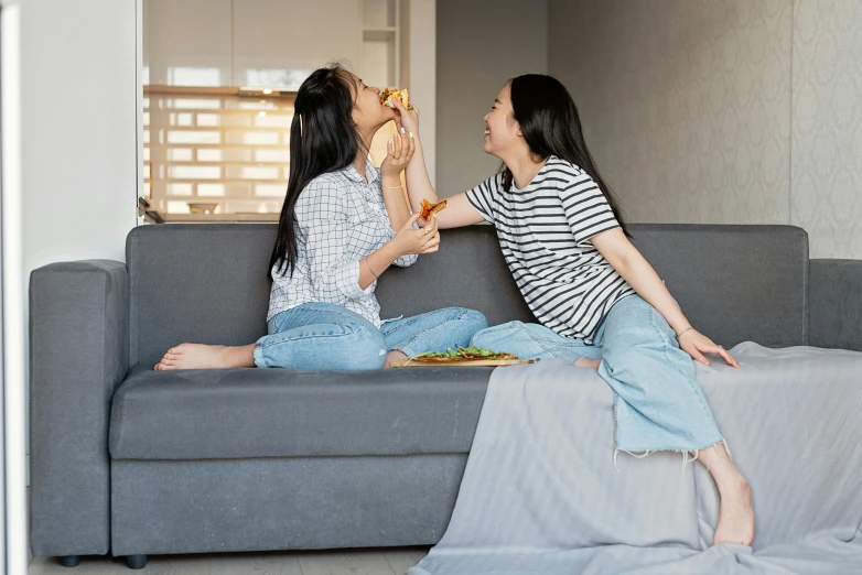 a couple of women sitting on top of a couch, pexels contest winner, munching pizza, asian female, grey, dancing with each other