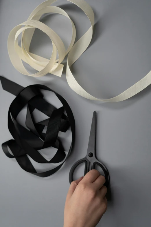 a person cutting a ribbon with a pair of scissors, by Haukur Halldórsson, visual art, product shoot, or black, big ribbon, silver，ivory