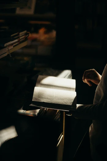 a person reading a book in a dark room, pexels contest winner, light and space, holy light, softly backlit, he is holding a large book, in a library