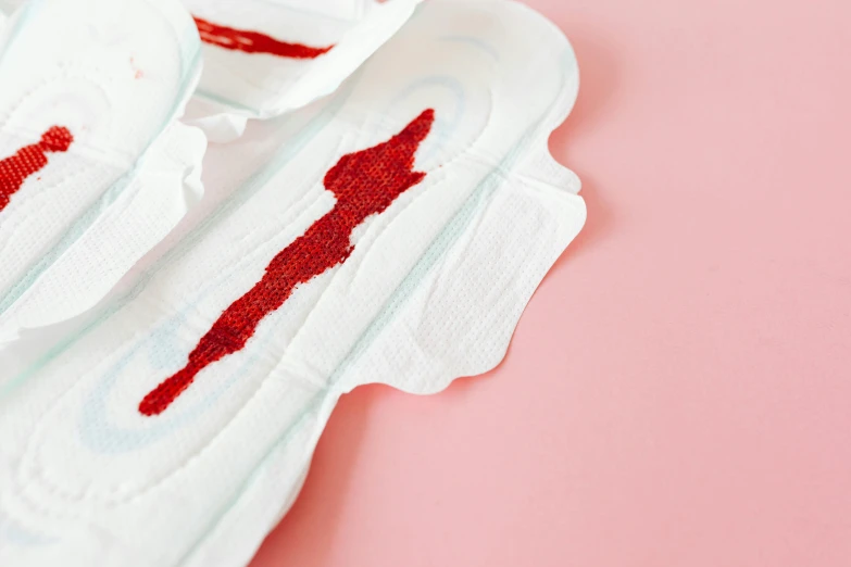 a pair of sanitary pads sitting on top of a pink surface, inspired by Louise Bourgeois, process art, dripping blood, close up shot from the side, trail of blood follows behind it, product design shot