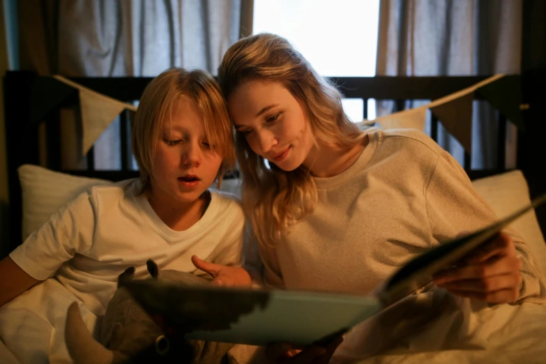 a couple of women sitting on top of a bed, by Lee Loughridge, pexels, realism, kid lit, trying to read, screenshot from a movie, with a kid