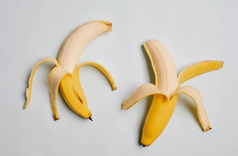 two peeled bananas sitting side by side on a white surface, by Carey Morris, trending on pexels, on grey background, 6 pack, two male, shrugging