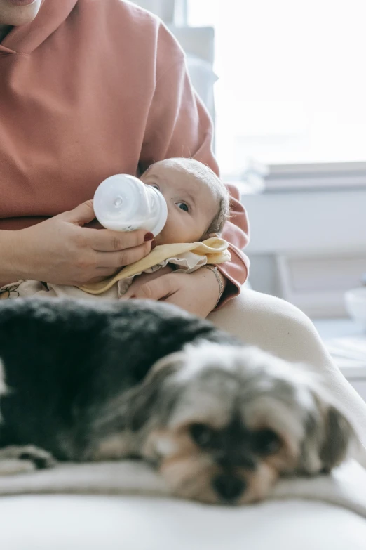 a woman sitting on a bed holding a baby and a dog, pexels contest winner, renaissance, holding a bottle, manuka, ready to eat, flowing milk
