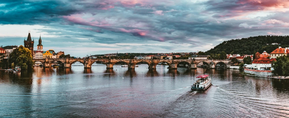a boat traveling down a river next to a bridge, by Matija Jama, pexels contest winner, art nouveau, brown and magenta color scheme, prague, panoramic shot, subtitles