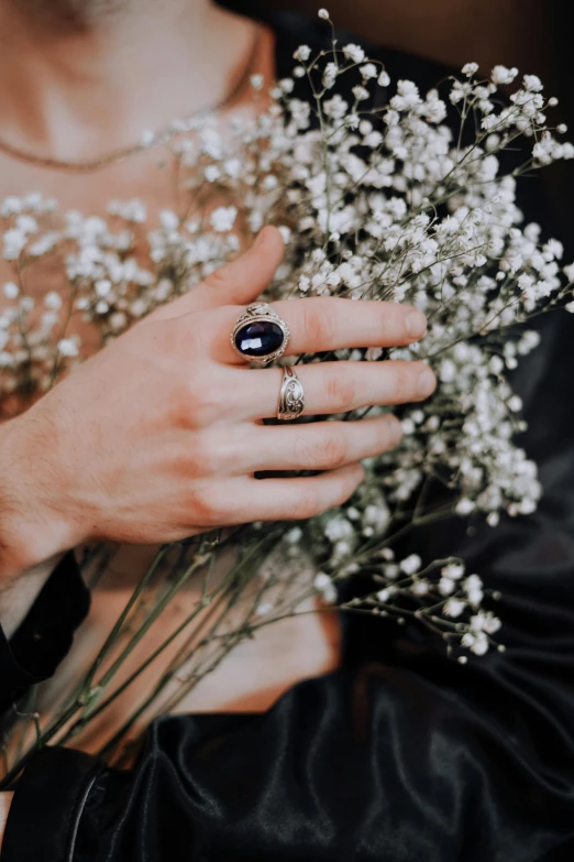 a woman holding a bouquet of white flowers, a black and white photo, by Lucia Peka, trending on unsplash, romanticism, blue jewellery, black magic crystal ring, carved from sapphire stone, dark blue clothes
