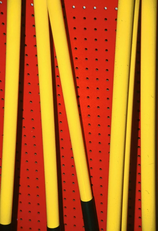 a bunch of baseball bats sitting on top of a red wall, inspired by Barnett Newman, op art, bright yellow color scheme, perforated metal, hoses, [ greg rutkowski ]