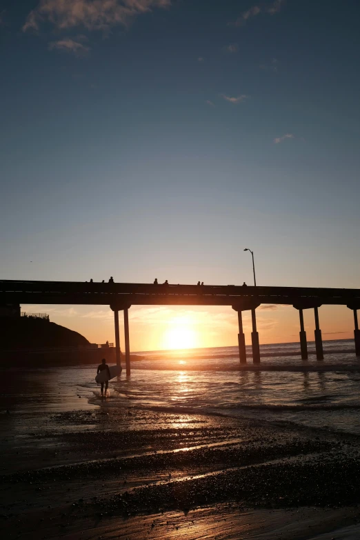 a man riding a surfboard on top of a sandy beach, bridge, ((sunset)), pch, over the shoulder