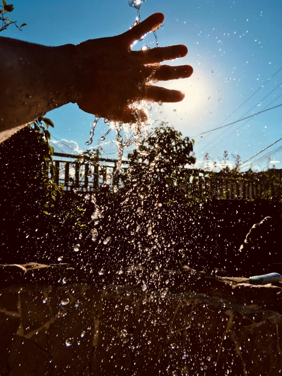 a person's hand is sprinkled with water, by Niko Henrichon, unsplash, happening, in the sun, low angle shot, promo image, taken in the late 2000s