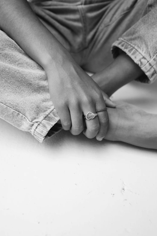 a black and white photo of a person with a ring on their finger, jeans and t shirt, in a chill position, legs intertwined, wearing jewelry