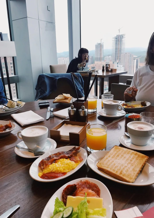 a group of people sitting at a table with plates of food, high rises, breakfast, instagram post, 8k octan photo