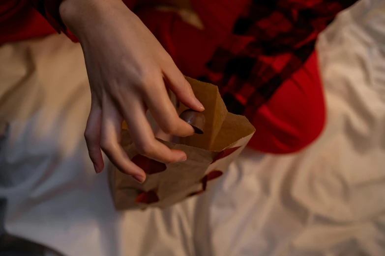 a person sitting on a bed holding a paper bag, by Julia Pishtar, pexels contest winner, christmas night, unclipped fingernails, crimson themed, holding hands