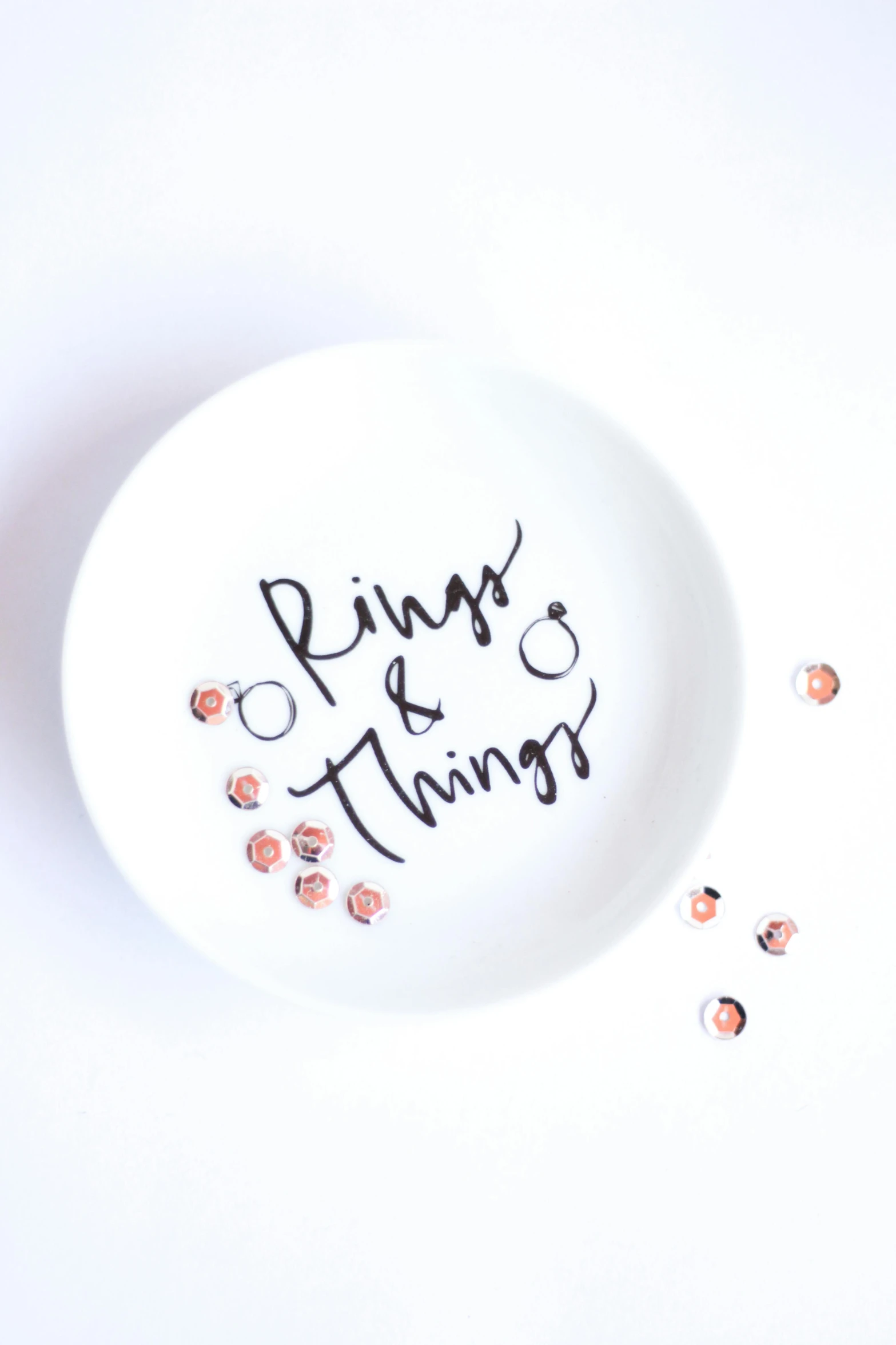 a white plate sitting on top of a table, inspired by Pieter de Ring, trending on unsplash, happening, etsy stickers, rings, flowing lettering, with sparkling gems on top