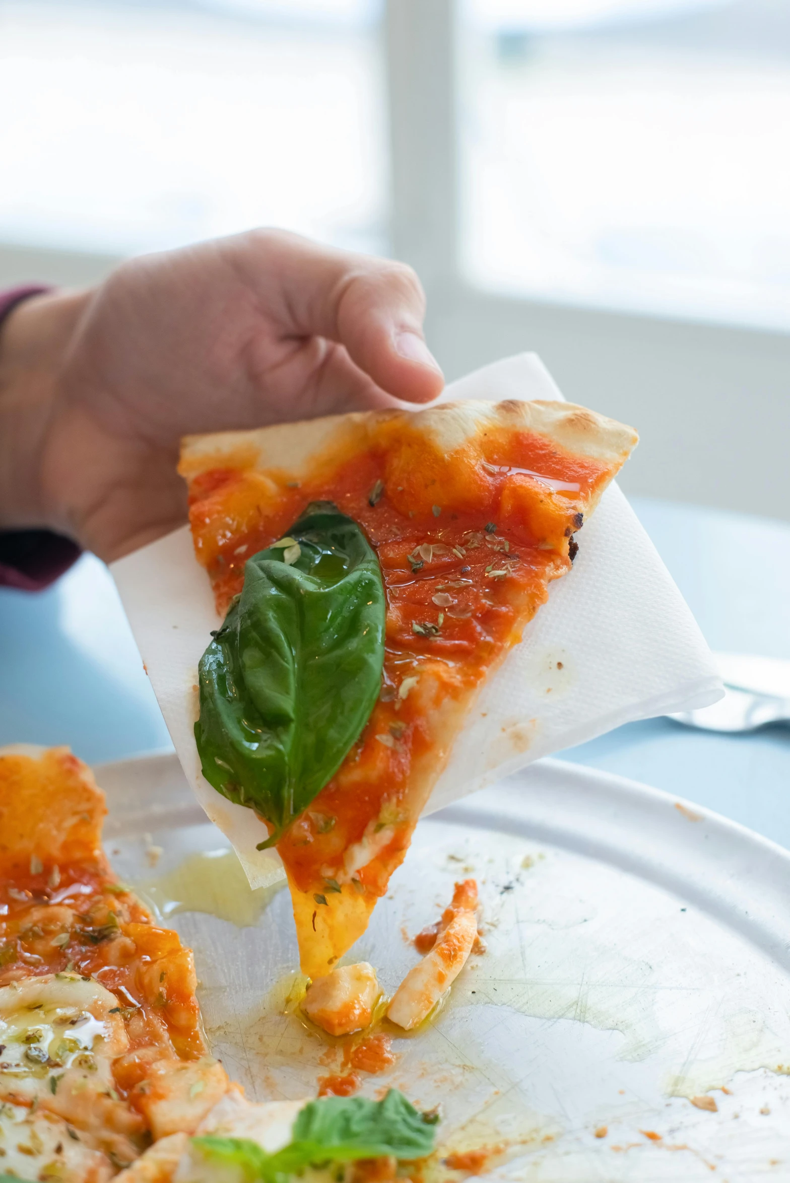 a person taking a slice of pizza from a plate, parchment paper, orange, basil, gooey