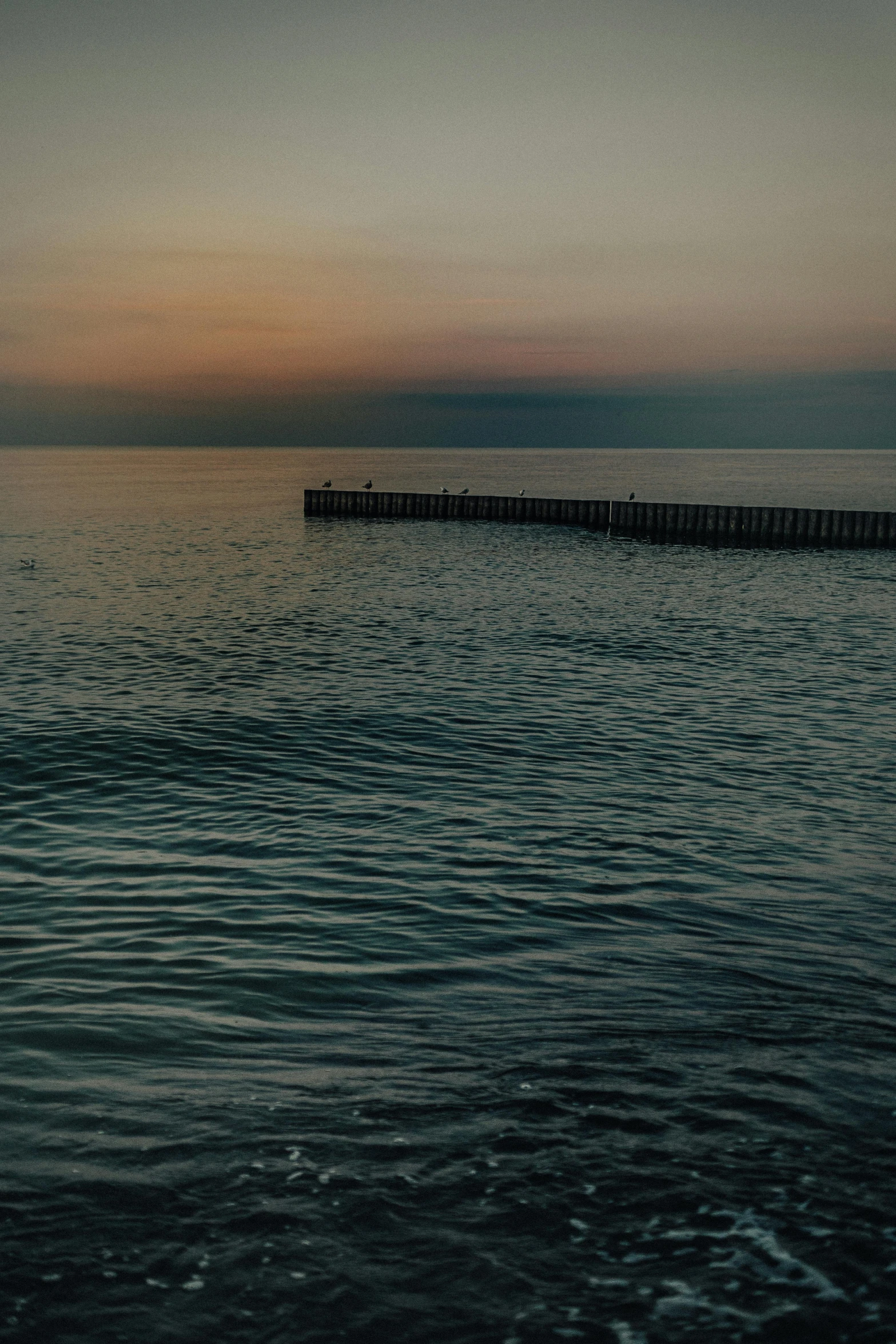 a body of water with a pier in the background, a picture, inspired by Elsa Bleda, unsplash, black sea, twilight ; wide shot, low quality footage, cinematic-shot