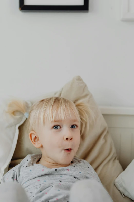 a little girl laying on top of a bed, pexels contest winner, spitting cushions from his mouth, vanilla, looking to the right, bedhead