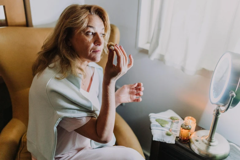 a woman sitting in a chair in front of a mirror, holding a candle, candy treatments, profile image, wrinkles