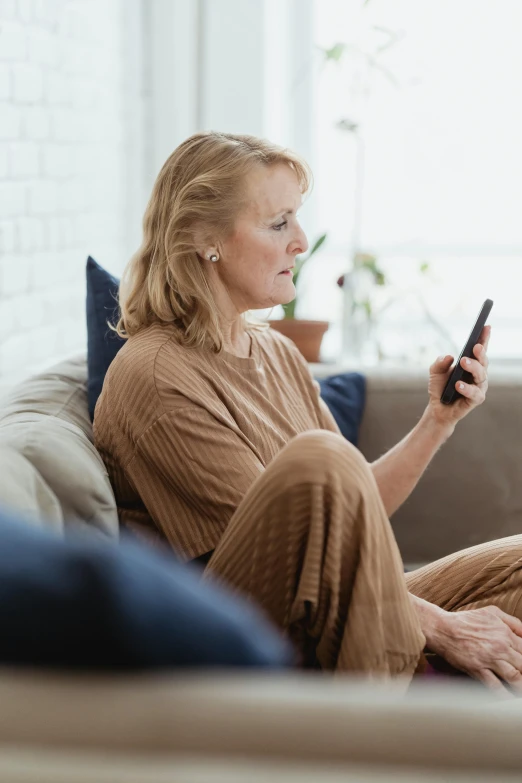 a woman sitting on a couch holding a cell phone, digital health, brown, older woman, instagram picture