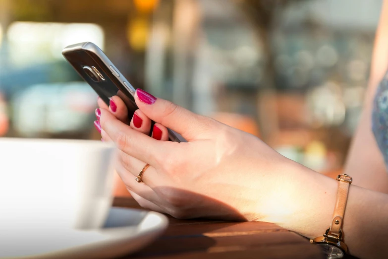 a close up of a person holding a cell phone, happening, sitting in a cafe, 9 9 designs, morning sun, 5 feet away