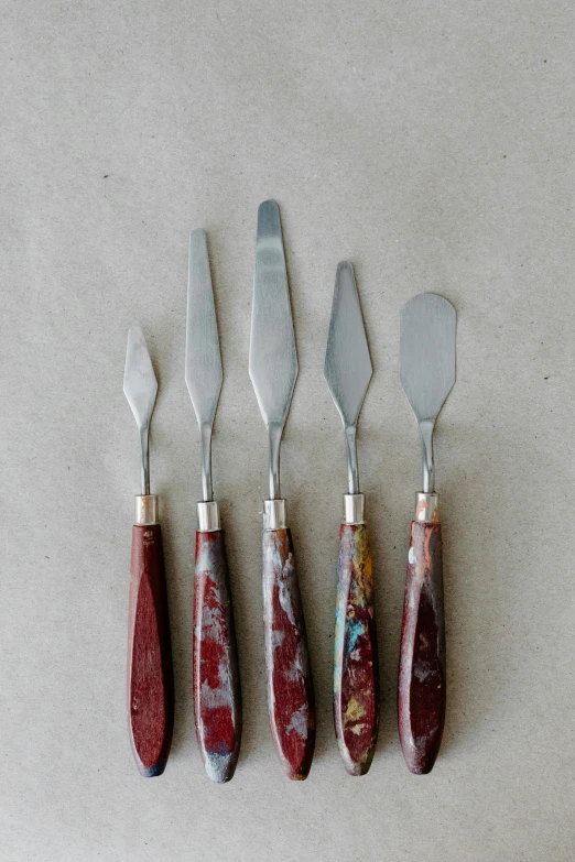 five knives sitting next to each other on a table, inspired by Stanley Spencer, baroque, long paint brush strokes, brown resin, silver and crimson ink, vintage shapes