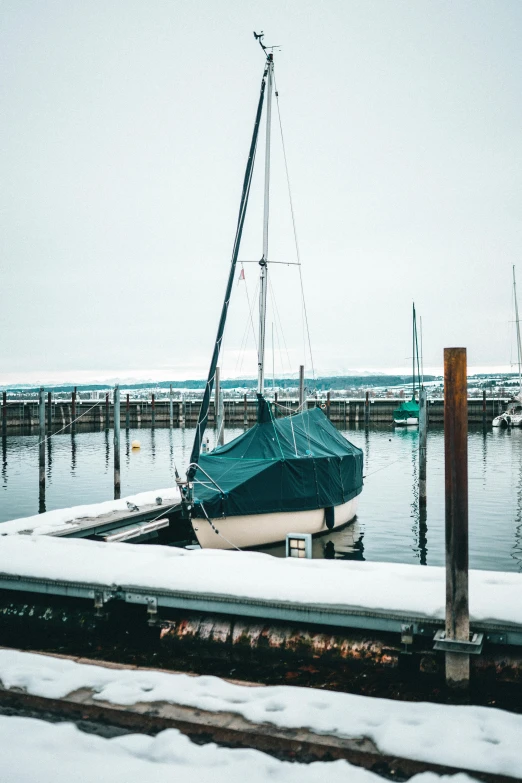 a boat sitting on top of a snow covered dock, sailboats in the water, it's raining outside, winter photograph, covered in