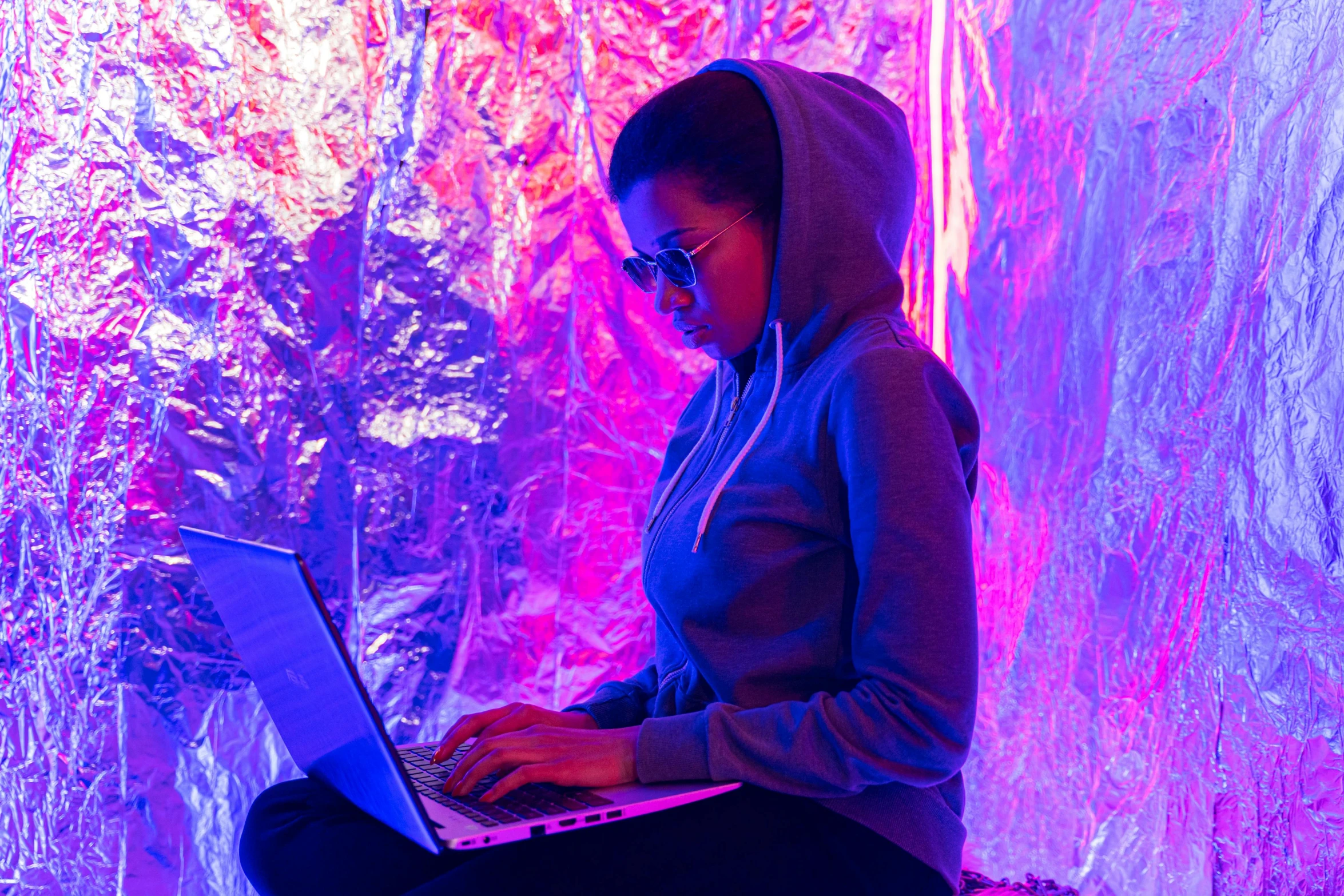 a woman sitting in front of a laptop computer, a hologram, unsplash, hydroponic farms, in an igloo, neon wiring, wearing space techwear