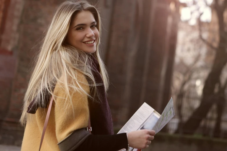 a woman walking down a street holding a book, pexels contest winner, happening, smiling fashion model, chloë grace moretz, post graduate, winter sun