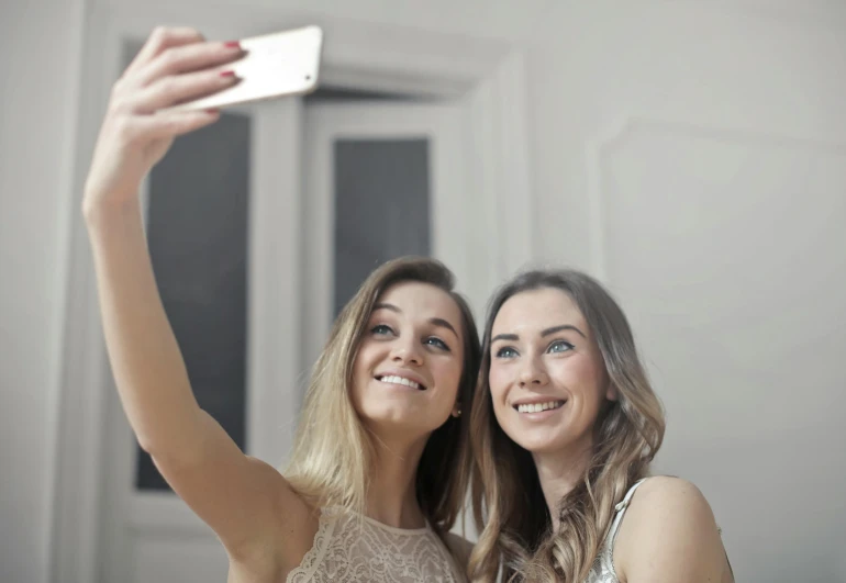 two women taking a selfie in front of a mirror, trending on pexels, one blonde and one brunette, teenage girl, looking straight into camera, good lighted photo