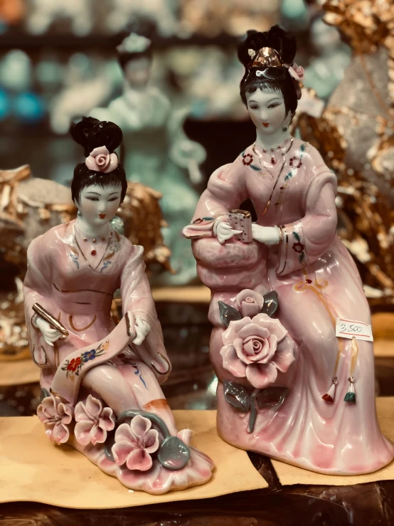 a couple of figurines sitting on top of a table, pink flowers, in style of lam manh, sitting on a store shelf, stunning and rich detail