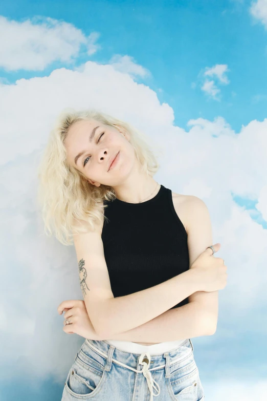 a woman leaning against a wall with her arms crossed, an album cover, inspired by Elsa Bleda, pexels contest winner, magic realism, standing on a cloud, portrait of elle fanning, happy clouds behind, she is wearing a black tank top