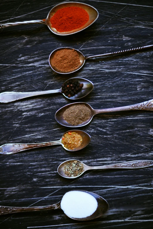 a group of spoons sitting on top of a wooden table, spices, charcoal and silver color scheme, thumbnail, cliffside