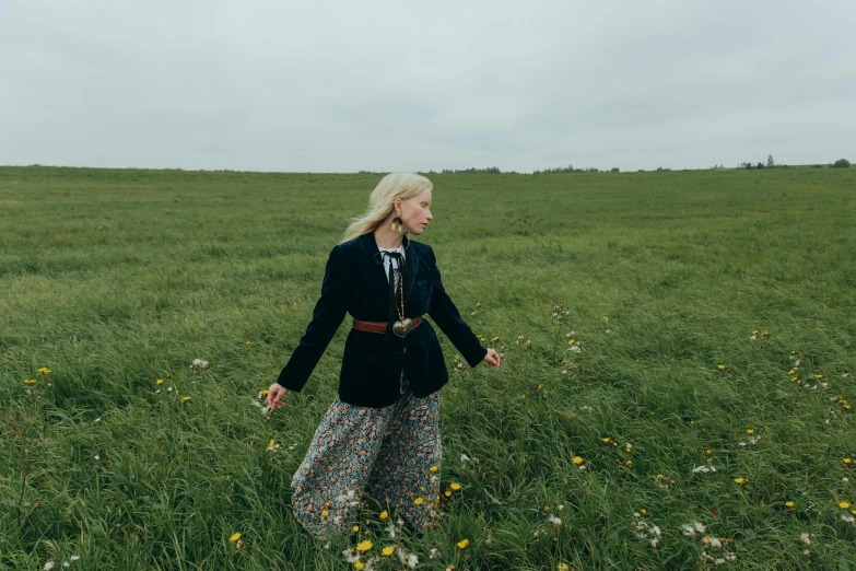 a woman walking through a field of tall grass, an album cover, inspired by Nína Tryggvadóttir, unsplash, wearing jacket and skirt, liz truss, press shot, mary anning