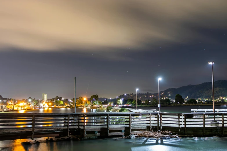 a bridge over a body of water at night, by Tom Bonson, pexels contest winner, harbour in background, bay area, slight overcast, distant mountains lights photo