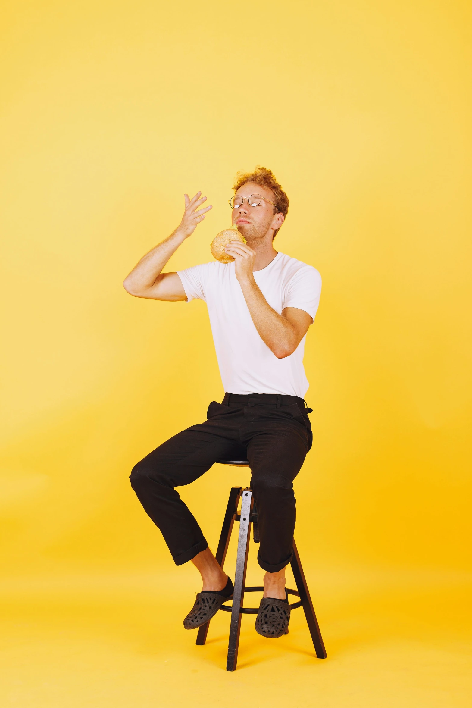 a man sitting on top of a stool, yellow backdrop, limmy, hand gestures, dustin lefevre