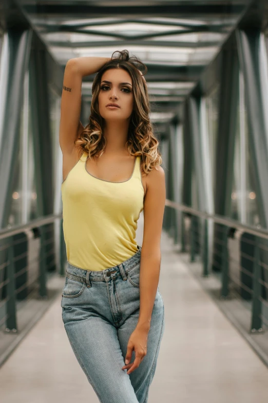 a woman posing for a picture on a bridge, a colorized photo, inspired by Elsa Bleda, pexels contest winner, wearing yellow croptop, jeans, attractive face and body, indoor picture