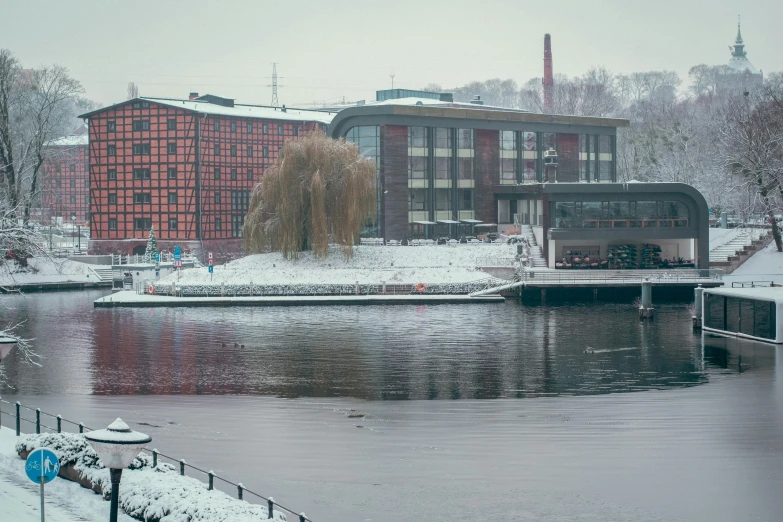 a body of water surrounded by snow covered trees, by Grytė Pintukaitė, pexels contest winner, modernism, industrial buildings, red brown and grey color scheme, viewed from the harbor, aardman studios