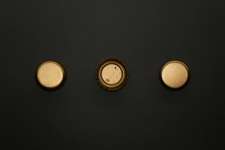 a close up of three buttons on a black surface, by Zoltán Joó, unsplash, conceptual art, beer bottles, gold crown, ignant, overhead view