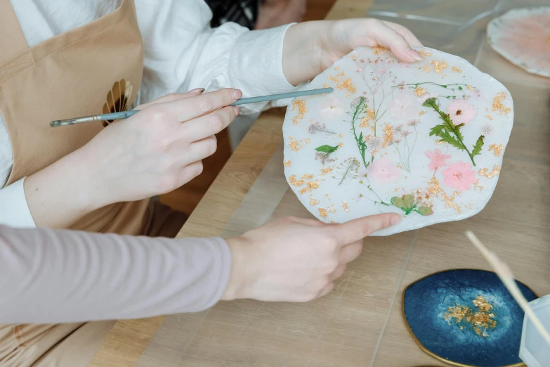 a close up of a person holding a plate with flowers on it, process art, resin, people at work, on a table, carefully crafted