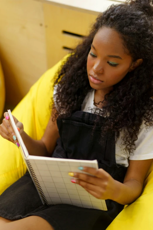 a woman sitting on a bean bag chair reading a book, a portrait, trending on unsplash, black teenage girl, writing on a clipboard, yellow and black color scheme, girl wearing uniform