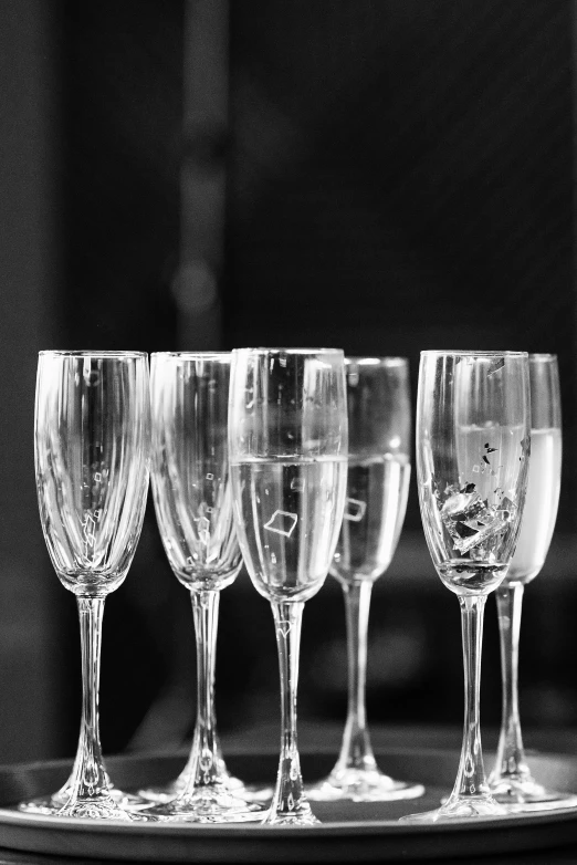 six empty wine glasses lined up on a tray, a black and white photo, by Caroline Mytinger, floating symbols and crystals, champagne, refracted line and sparkles, cocktail in an engraved glass