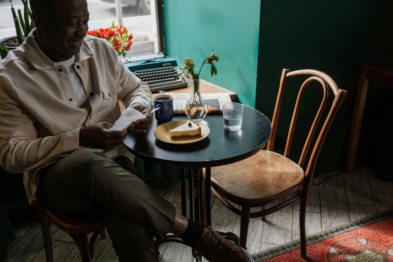 a man sitting at a table in front of a typewriter, by Emma Andijewska, pexels contest winner, inside a french cafe, ethiopian, sitting on a mocha-colored table, ignant
