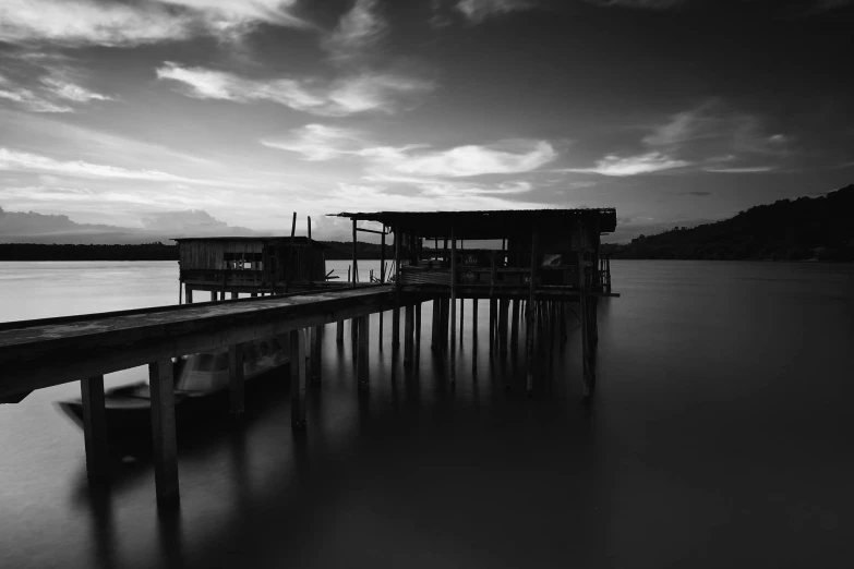 a black and white photo of a dock, a black and white photo, unsplash, houses on stilts, sunset dark dramatic day, long exposure 8 k, skins