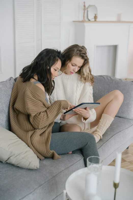 two women sitting on a couch looking at a tablet, trending on pexels, aestheticism, lesbian embrace, professional photo, grey, asian women