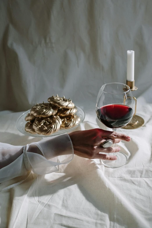 a close up of a person holding a glass of wine, a still life, inspired by Bourgeois, pexels contest winner, romanticism, golden accents, pastries, slightly minimal, dinner table